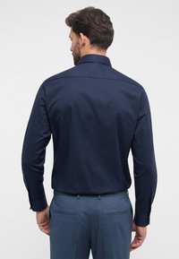 Marineblaues Langarmhemd mit einem Kentkragen, glatter Textur und Knopfmanschetten, kombiniert mit hellblauen maßgeschneiderten Hosen.
