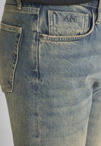 Jeans de mezclilla azul claro con una textura desgastada. Presenta un bolsillo trasero con un logo grabado y un diseño clásico de cinco bolsillos.