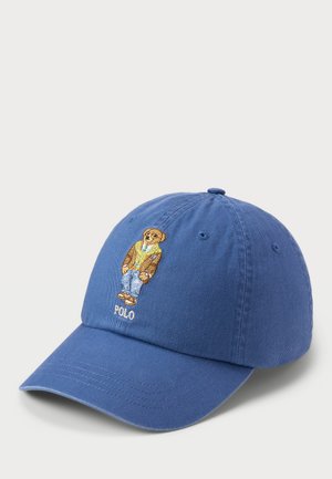 Kék pamut sapka ívelt vízszintes karimával. Hímzett medvével, aki pulóvert, farmert és szandált visel, alatta a "POLO" felirattal.