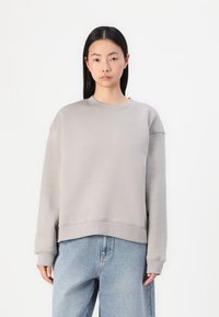 Lys grå sweatshirt med rund hals og senkede skuldre. Laget av mykt stoff, med en avslappet passform og ribbestrikkede mansjetter.