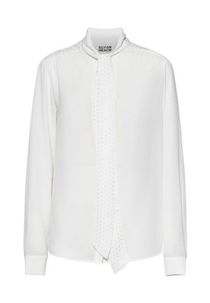 Blusa bianca a maniche lunghe con collo alto e cravatta annessa con piccoli puntini neri, etichettata Silvian Heach.