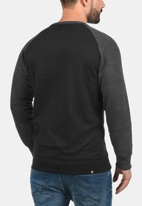 Sudadera negra con mangas raglán grises, puños y dobladillo acanalados, material de algodón, diseño liso, sin gráficos ni patrones visibles.