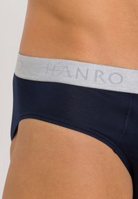 Navyblauwe slip van zachte stof met een lichtgrijze elastische tailleband met het "HANRO"-logo. Het ontwerp heeft naadloze randen voor comfort.