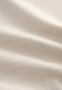 Tela de jersey de algodón en un suave color beige, con una textura lisa, un ligero estiramiento y un tejido uniforme y consistente en toda su superficie.