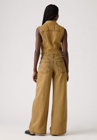 Tan denim jumpsuit met mouwloos ontwerp, wijdere broekspijpen, gestructureerde kraag en achterzakdetails. Soepele textuur, casual pasvorm.