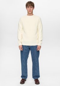 Kremfarvet, ribstrikket sweater med rund hals, kombineret med løstsiddende blå denimjeans og brune lædersko.