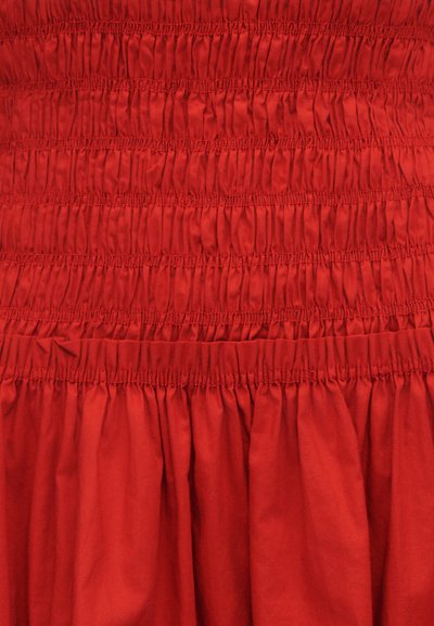 Κόκκινο βαμβακερό φόρεμα με κορσάζ σμόκινγκ με ρυτιδιασμένη υφή και φουσκωτή φούστα. Ομαλή, ελαφρώς γυαλιστερή επιφάνεια με ελαστικές λεπτομέρειες.