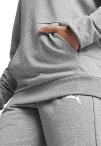 Felpa grigia con tasca frontale e polsini a costine, abbinata a pantaloni jogger grigi con un logo bianco sulla coscia.