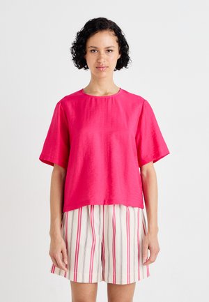 Haut fuchsia à manches courtes en tissu léger, avec un col rond et une coupe décontractée, associé à un short rayé rose et blanc.