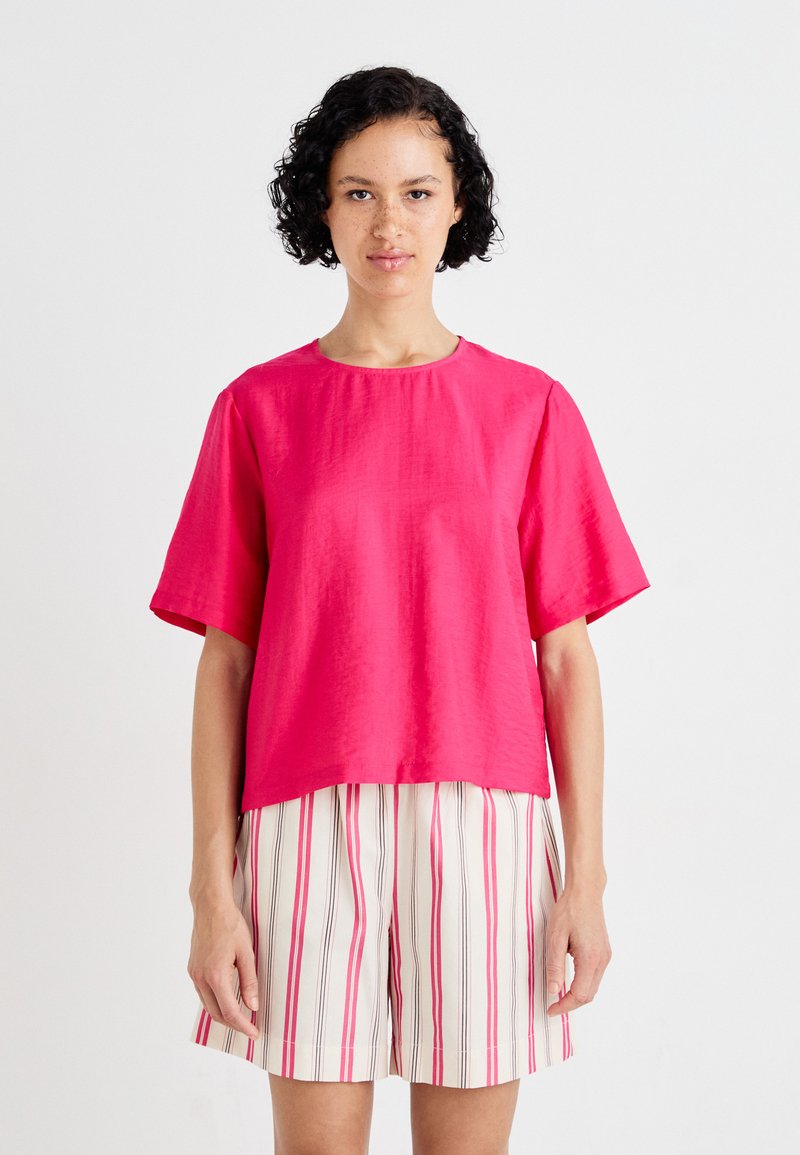 Fuchsia short-sleeve top made of lightweight fabric with a round neckline and relaxed fit, paired with striped shorts in pink and white.