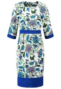 Robe fleurie mi-longue en tissu blanc, avec des accents bleus aux poignets et à la taille. Motif floral vibrant en tons rouges, bleus et verts.