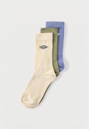 Trois paires de chaussettes montantes côtelées en beige, vert olive et bleu, chacune arborant un petit logo Dickies sur le revers.