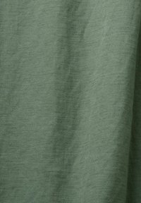 Gros plan sur un tissu vert texturé avec un motif de tissage visible et des plis subtils créant de douces ombres.