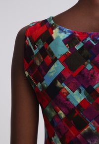 Buntes ärmelloses Kleid mit einem geometrischen Muster in Rot, Blau und Schwarz, aus glattem Stoff mit rundem Ausschnitt.