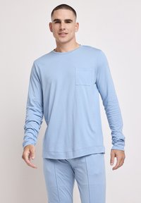 Langærmet lyseblå skjorte lavet af blødt stof, med en rund halsudskæring og en brystlomme, båret med matchende lyseblå bukser.