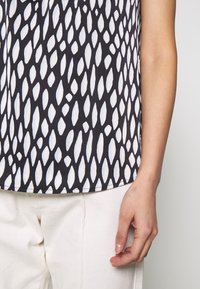 Kortärmad blus med ett svart och vitt mönster av avlång form, tillverkad av lättviktsmaterial med en slät yta.