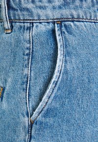 Světle modré džíny z denimu s přední kapsou, kontrastním prošitím a mírně opotřebovanou strukturou. Zaměření na tkaní látky a tvar.