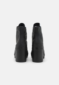 Black ankle boots with a textured leather finish, featuring a thick block heel and circular emblem accents on the rear.