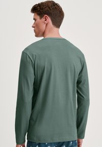 Lange mouw shirt in gedempte groene katoen met een ronde hals. Heeft een gladde textuur en een losse pasvorm. Draagt met een gestreepte pyjamabroek.