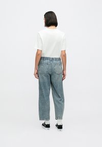 Blugi din denim albastru, cu croială lejeră și talie elastică, cu buzunare posterior; asortați cu un tricou simplu alb cu mâneci scurte și adidași negri.