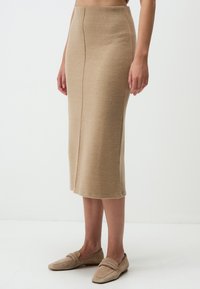 Beige gestrickter Bleistiftrock mit gerader Silhouette, der über ein dezentes Nahtdetail und einen mittellangen Schnitt verfügt, kombiniert mit passenden Slippern.