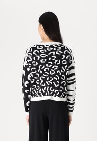 Pull en tricot noir et blanc avec un imprimé léopard au dos et un motif rayé sur les manches. Ourlets et poignets côtelés.