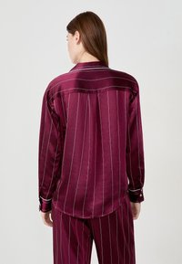 Bordowa satynowa koszula w białe paski, z długimi rękawami, kołnierzykiem i mankietami na guziki; gładka tekstura i luźny krój, w połączeniu z pasującymi spodniami.