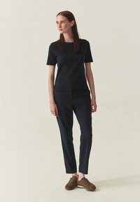 T-shirt bleu marine et pantalon sur mesure en tissu à texture lisse. Baskets marron avec lacets et détails de surpiqûres discrètes.