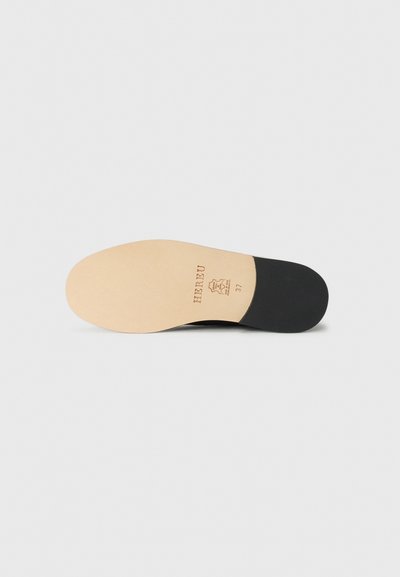 Semelle de chaussure noire avec un centre beige clair, marquée "HIREU" et taille "37", présentant une texture lisse et une légère courbure.