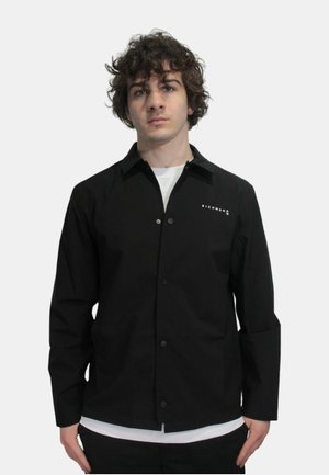 Giacca nera con bottoni realizzata in tessuto leggero, con maniche lunghe. Presenta un piccolo logo bianco sul lato sinistro del petto e un design classico del colletto.