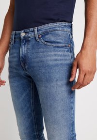 Fadade blå denimjeans med en slim fit, med en klassisk femfickorsdesign och kopparfärgade sömnadsdetaljer.