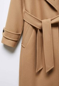 Płaszcz w kolorze kamelowym o teksturowanej tkaninie, z szerokim kołnierzem, paskiem w talii i detalami z guzikami na mankietach.
