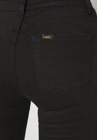 Jeans negros hechos de una mezcla de algodón, con una etiqueta amarilla "Lois" en el bolsillo trasero y un diseño de acento en hilo plateado.