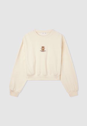 Kremowy, skrócony sweatshirt z długimi rękawami i ściągaczami. Na klatce piersiowej znajduje się brązowy haftowany miś oraz napis. Miękka tekstura.