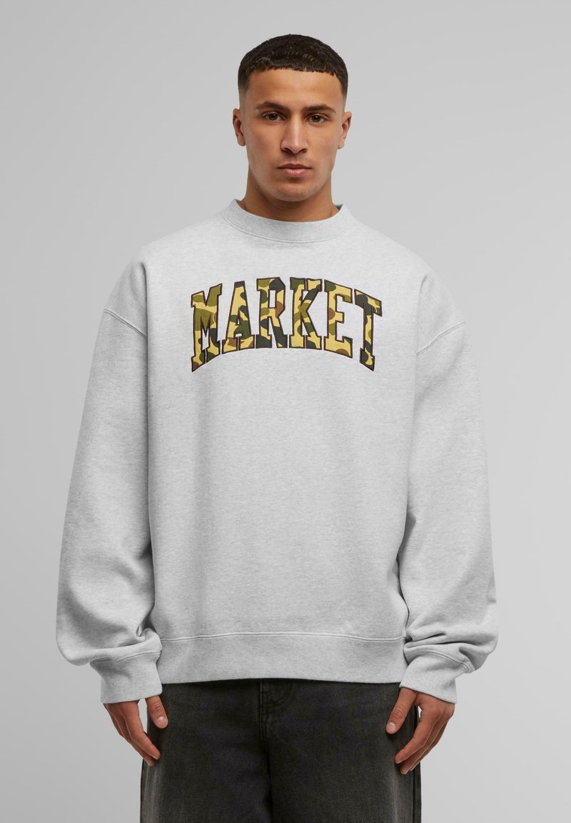 Szürke pulóver lekerekített nyakrésszel és oversized fazonnal. "MARKET" felirat kamuflázs mintával a mellkason. Rugalmas mandzsetták és alj.