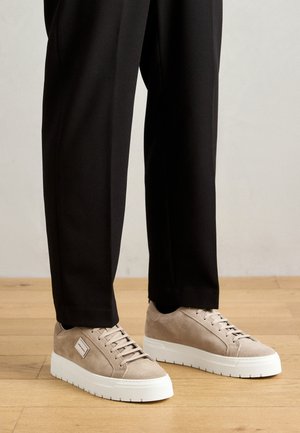 Beige suede sneakers met witte rubberen zolen, ronde neus en vetersluiting. Gepaard met zwarte op maat gemaakte broeken. Gladde textuur en minimale accenten.