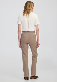 Kremowa bluzka z krótkim rękawem i zamkiem z tyłu; beżowe slim-fit spodnie o gładkiej fakturze; kapcie w leopardzi wzór.