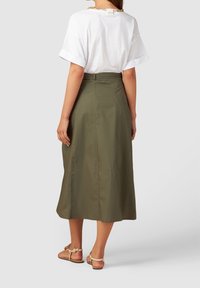 Olijfgroen maxi-rok met een gladde textuur, hoge taille en een split aan de achterkant. Gepaard met een losvallend wit T-shirt en tan sandalen.