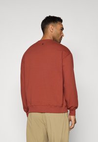 Felpa color ruggine in cotone con colletto a girocollo, polsini a costine e orlo, con un piccolo dettaglio a stella sul retro.