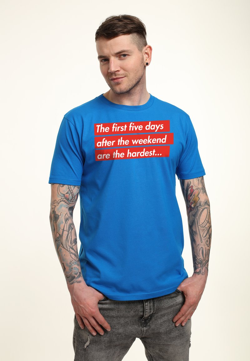 Camiseta de algodón azul con mangas cortas que presenta texto rojo: "Los primeros cinco días después del fin de semana son los más difíciles..." en la parte frontal.