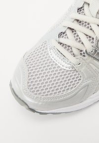 Partie avant d’une chaussure de sport blanche en tissu mesh, avec des renforts synthétiques et des lacets blancs sur fond blanc.