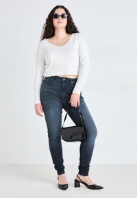 Λευκό κοντό μακρυμάνικο μπλουζάκι, σκούρο μπλε εφαρμοστό τζιν, μαύρη τσάντα ώμου με γυαλιστερή υφή και μαύρες ψηλοτάκουνες παπούτσες με μυτερές μύτες.