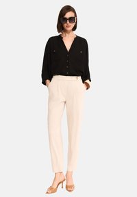 Czarna koszula z guzikiem o luźnym kroju, kremowe spodnie z przodu z zakładkami i detalem guzika oraz tanie sandały na obcasie.