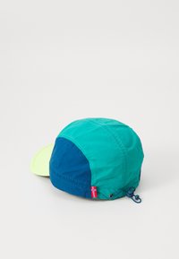 Krāsains cepures ar zaļo un zilo paneļu maisījumu, gaiši zaļa mala, regulējama aukla un neliela karoga akcenta detaļa sānos.