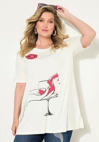 Vit t-shirt med en grafik av en hand som håller ett glas med röd vätska, accentuerad av röda läppar ovanför designen. Korta ärmar och avslappnad passform.