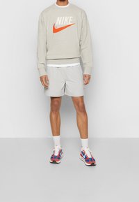 Ljusgrå sweatshirt med orange Nike-logotyp, grå rutiga shorts och flerskadiga Nike-sneakers med röda, blå och vita accenter.