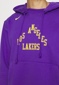 Sweat à capuche violet avec logo Nike jaune et texte "Los Angeles Lakers" sur la poitrine en lettres jaunes.