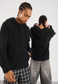 Zwarte gebreide hoodie met een textuurpatroon, voorzak en koordjes. Gekocht met een geruit broek en losse jeans.