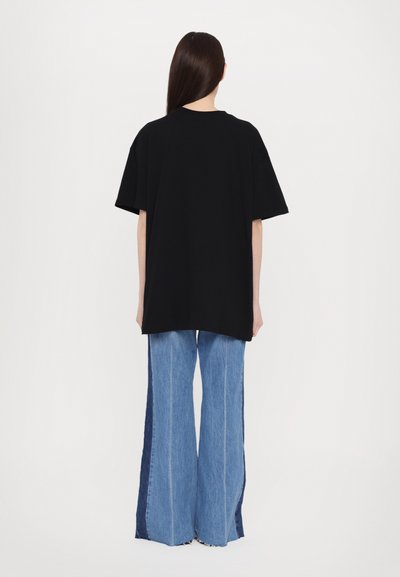 Camiseta oversized negra de manga corta, combinada con unos vaqueros de pierna ancha de tiro alto en un azul claro, con paneles oscuros a los lados y dobladillo deshilachado.