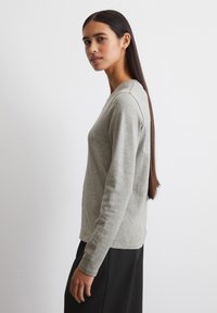 Lys grå langærmet top lavet af et blødt stof, med en rund halsudskæring og afslappet pasform. Designet er minimalistisk uden yderligere mønstre.